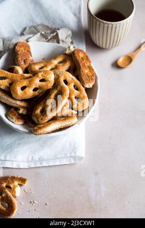 From above bunch of fresh tasty pretzels served in bowl near napkins and cup of coffee on gray table during breakfast in morning Stock Photo