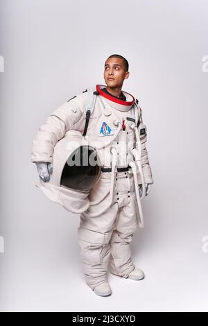 Astronaut in spacesuit taking off protective helmet with visor in studio against white background Stock Photo