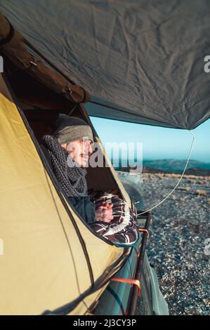 Focused male freelancer in casual outfit sitting on floor near window and typing on laptop while working remotely from home Stock Photo