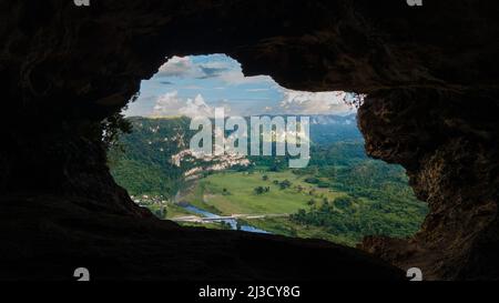 View through hole on rocky cliffs covered with green trees and river flowing through valley Stock Photo