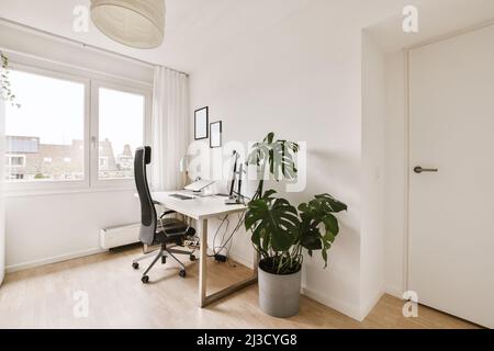 Office chair placed at wooden table with computer screen in spacious white room in flat designed in minimal style Stock Photo