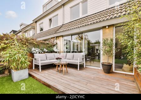 Cozy wooden table and soft sofa placed in backyard with green garden near contemporary residential building Stock Photo