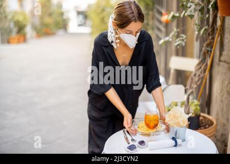Woman takes off face mask while sitting at italian restaurant outdoors Stock Photo