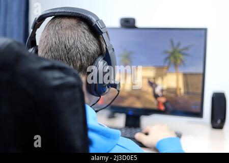 Man in headset playing a computer game on desktop PC. Concept of game addiction, home leisure Stock Photo