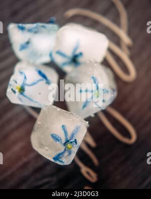 Frozen flowers for body care on wooden surface. Fresh skin concept. Creative composition with blue petals frozen in ice cubes. Stock Photo