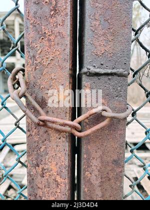 Close-up of a chain hangs on a rusty wire fence. The background is blurry Stock Photo