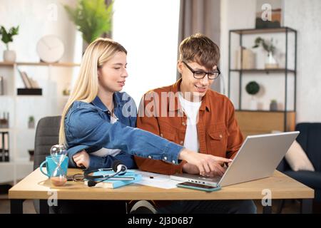 Male and female young business partners in casual wear discussing common project at bright modern office. Caucasian colleagues freelancers using laptop for work. Stock Photo