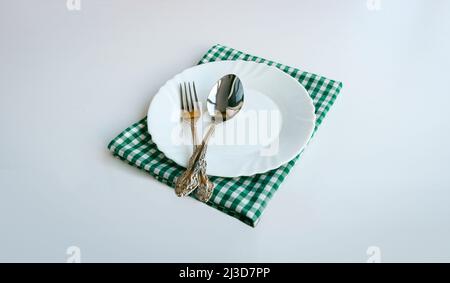 White plate, cutlery and checkered doily on a light background. Stock Photo