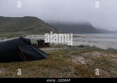 Tent on a beach in Lofoten, Norway during stormy and rainy weather with foggy mountains in the background Stock Photo