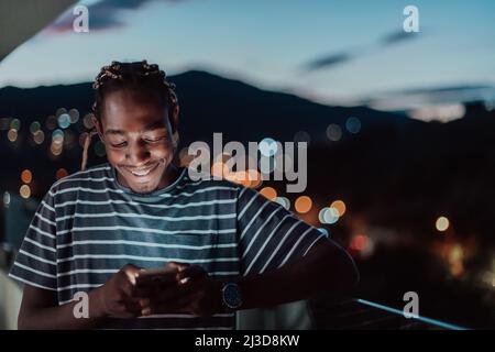 The young man on an urban city street at night texting on smartphone with bokeh and neon city lights in the background.  Stock Photo