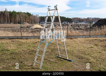 A tall, fold-out aluminum ladder standing in the yard, in the shape of a triangle. Stock Photo