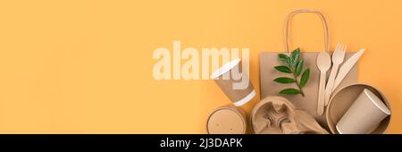Banner with eco-friendly tableware - kraft paper food utensils, paper containers and cups, drinking straws and wooden cutlery on orange background wit Stock Photo
