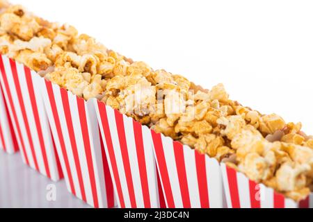 Popcorn boxes with white and red stripes full of sweet with caramel popcorn on white reflective background in white background with copy space. Select Stock Photo