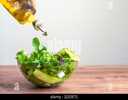 Close up photo of fresh mediterannean salad  on wooden table and hand pouring olive oil. Concept of mediterannean died as a lunch. Stock Photo
