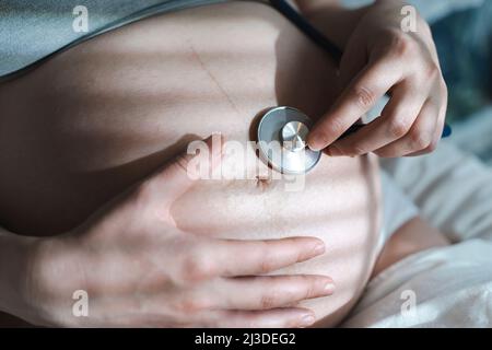 Pregnant woman listens to the baby heartbeat and movements with a stethoscope or fetoscope or Pinard Horn. Prenatal fetal health, anxiety, fear concept. High quality photo Stock Photo