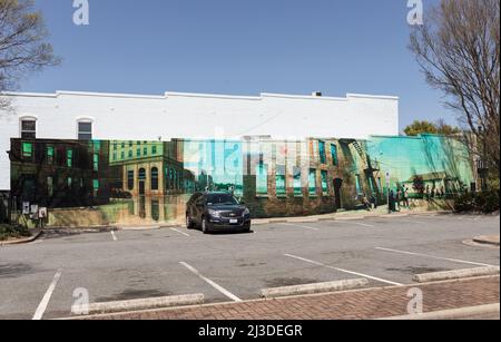 CONCORD, NC, USA-3 APRIL 2022: Parking lot with adjacent brick building wall containing mural of familiar downtown scenes. Stock Photo