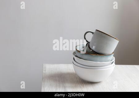 A pyramid of white bowls, plates and cups of different sizes and colors on a beige table in the kitchen. Scandinavian style. Place for your text. Copy Stock Photo