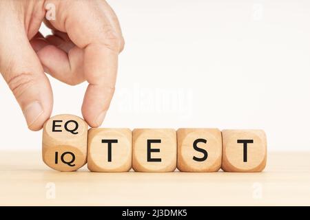 Hand flipping a wooden block with eq test and iq test phase. Copy space. White background Stock Photo