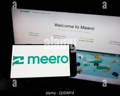 Person holding cellphone with logo of French photography company Meero on screen in front of business webpage. Focus on phone display. Stock Photo