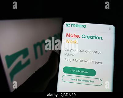 Person holding smartphone webpage logo of French photography company Meero on screen in front of logo. Focus on center of phone display. Stock Photo