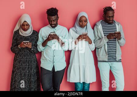 A group of African Muslim students use smartphones while standing in front of a pink background Stock Photo