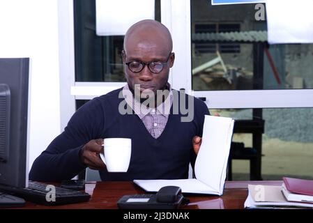 serious adult businessman sitting at desk looking at document while holding cup of coffee in hand. Stock Photo