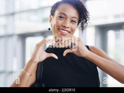 I love business. Cropped shot of a young businesswoman showing a heart sign while walking through a modern office. Stock Photo