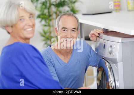 happy senior woman smiling while man in using the washing-machine Stock Photo