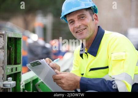 cheerful engineer with clipboard wearing reflective vest on construciton site Stock Photo