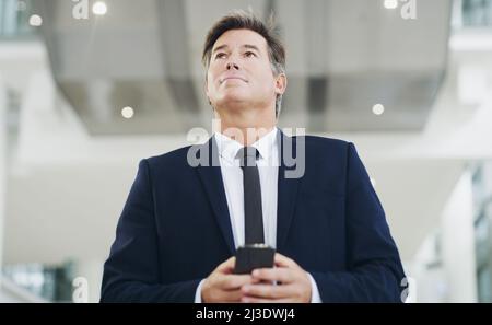 He's always thinking. Cropped shot of a mature businessman using a smartphone while walking through a modern office. Stock Photo
