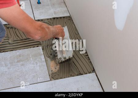 Construction workers laying tile over concrete floor using tile levelers, notched trowels Stock Photo