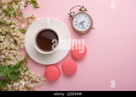 Spring floral background with coffee and macaroons, and alarm clock. Flat white flowers on a light pink background, top view, copy space. Stock Photo