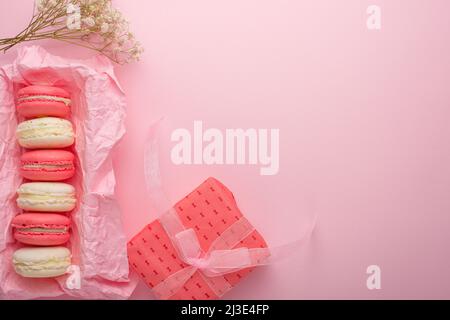 Macaroons in a box on a light pink background with a gift, flatlays, with an empty space for an inscription or congratulations on a holiday, a woman o Stock Photo