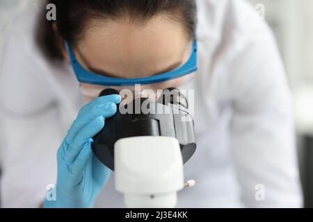 Woman doctor scientist looking through microscope in clinic Stock Photo