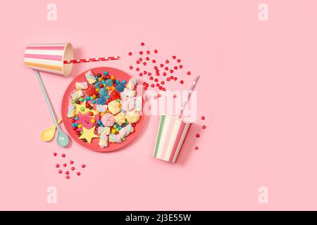 Colored meringues and candies in a pink plate and disposable cups on a pink background Stock Photo