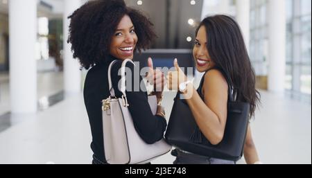 We're good to go. Cropped shot of two young businesswomen giving you a thumbs up while walking in an office. Stock Photo
