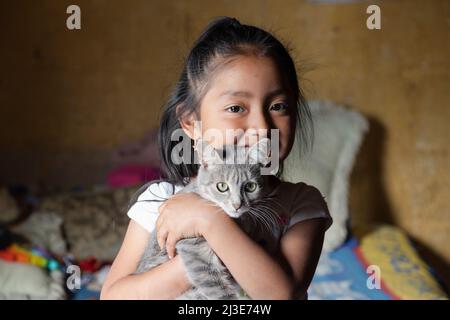 Little girl hugging her cat - Hispanic girl at home with her pet Stock Photo