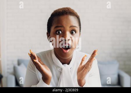 Surprised black woman sitting at office desk, looking at camera and clapping hands. ow face expression. Business concept. Shock news. Businesswoman Stock Photo