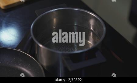 Water in pot is on the stove. ART. Water is being prepared for boiling in metal saucepan. Pots without lids on the stove Stock Photo