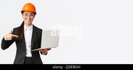 Smiling pleased asian female chief engineer showing chart with enterprise profit, making presentation during investors meeting, wearing safety helmet Stock Photo