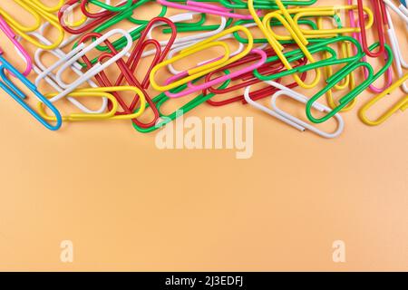 Multicolored Paperclips Isolated on a Cheerful Orange Beige Background with Copy Space on Bottom Stock Photo
