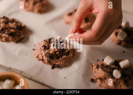 Close-up image, Female hands adding some marshmallow on a chocolate cookies dough. Baking concept. Stock Photo