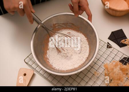 Top view, Female using a whisk to stir cookie flour with a chocolate cookie dough in the mixing bowl. Female cooking a cookies. Stock Photo
