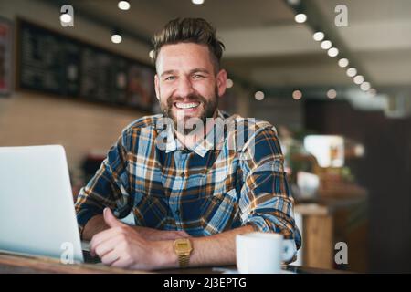 I like my internet connection as strong as my coffee. Portrait of a young man using his laptop while sitting by the window in a cafe. Stock Photo