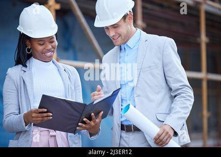 These plans look good. Shot of two coworkers looking over plans at a construction site. Stock Photo