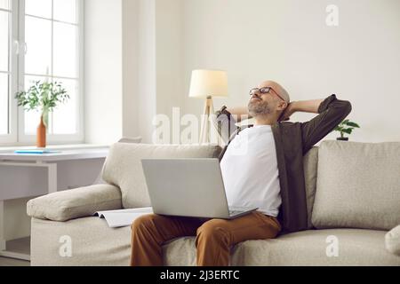 Smiling man puts his hands behind his head taking break after working with laptop. Stock Photo