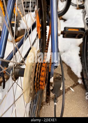 Blue bike has been outside all winter and got broken. Rusty bicycle chain hangs on sprocket and gear. Stock Photo