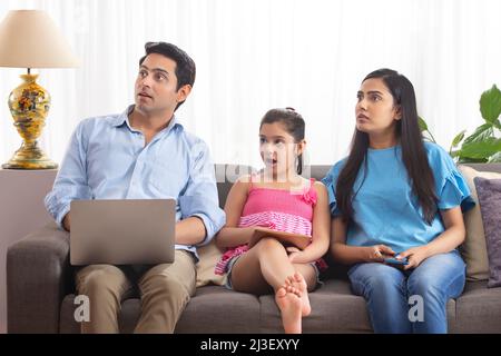 Family members looking elsewhere while sitting on sofa in living room Stock Photo