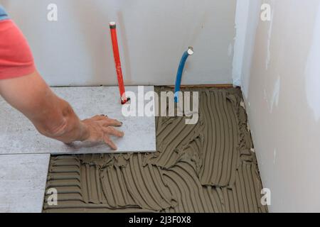 Tiler placing porcelain tile in position over adhesive Stock Photo
