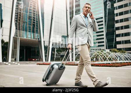 Ive landed and Im ready to talk business. Shot of a mature businessman talking on a cellphone while walking with a suitcase in the city. Stock Photo